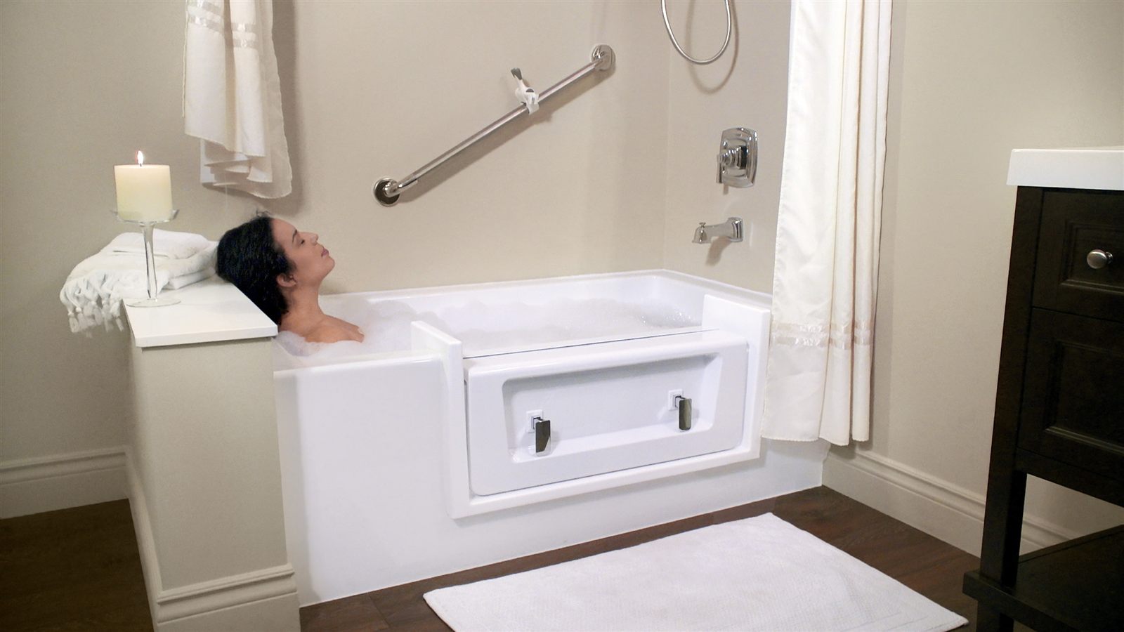 A woman relaxing in a full bubble bath with the cap in place and a grab bar on the wall