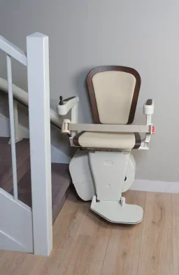 A cream stairlift folded compactly at the foot of the stairs