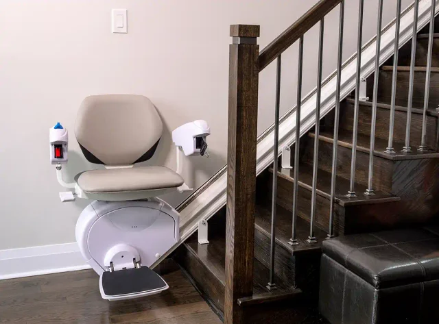 A beige straight stairlift beside a dark wood staircase
